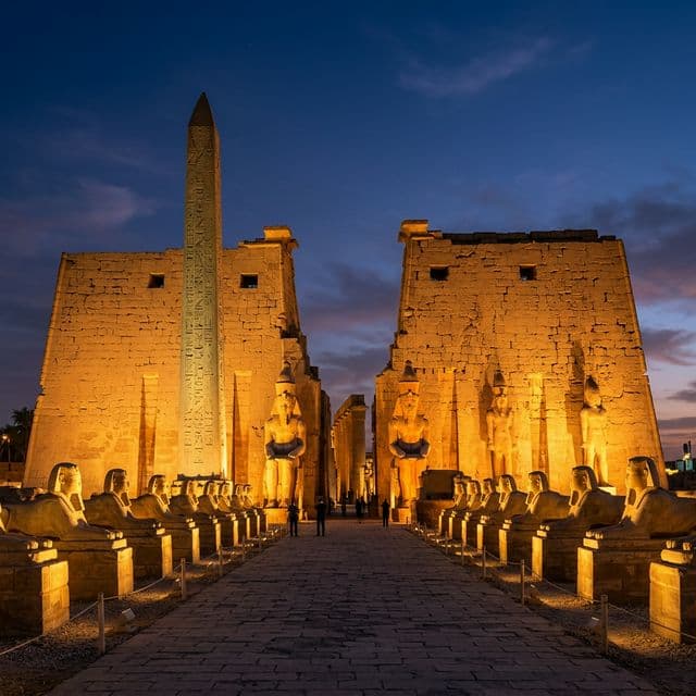 Luxor Temple illuminated in golden light at dusk with ancient obelisk and sphinx statues